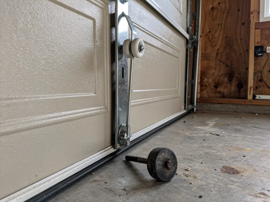 A garage door with a detached roller on the concrete floor.